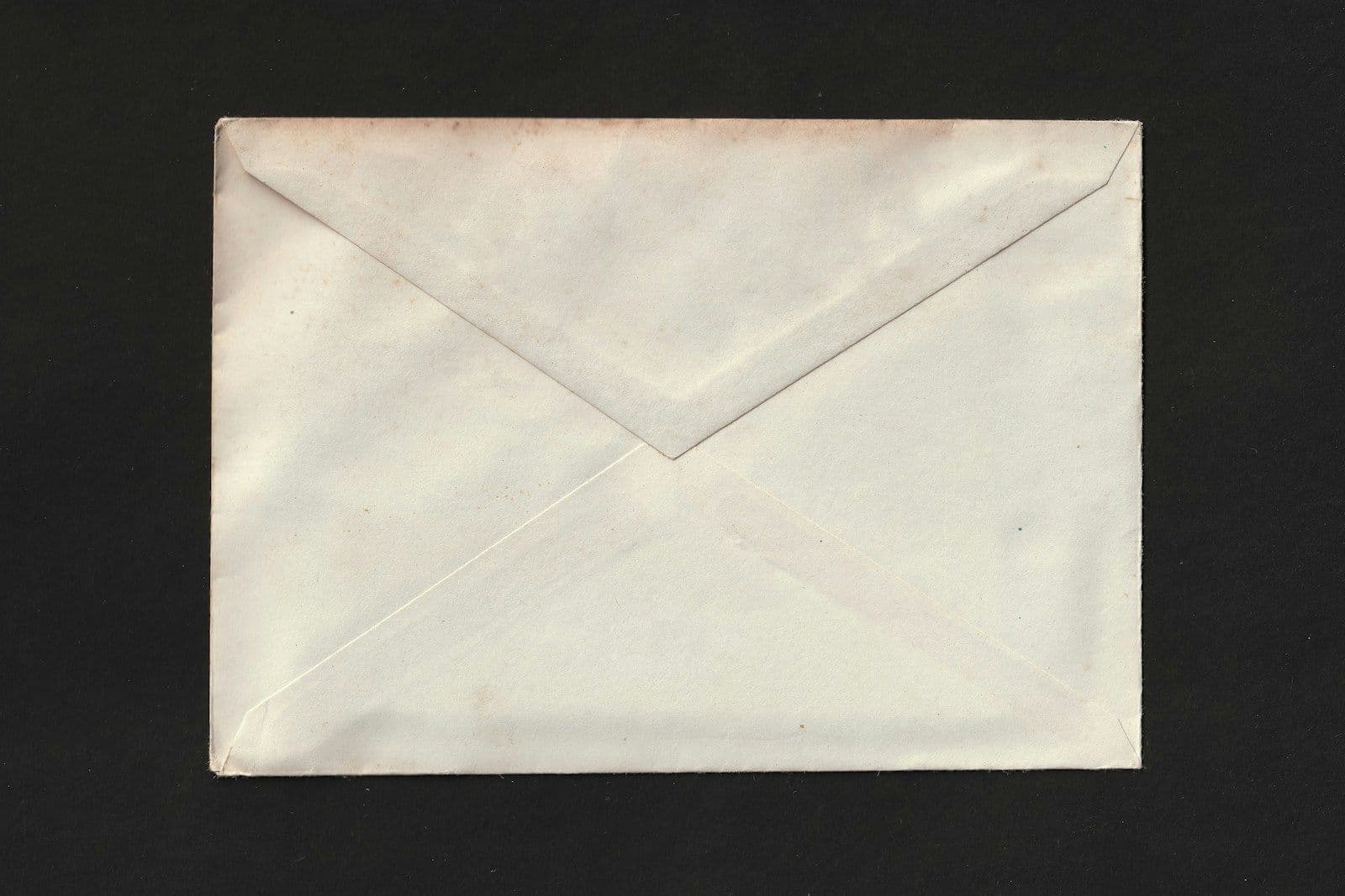 Blank white envelope with its flap side up, photographed against a black background