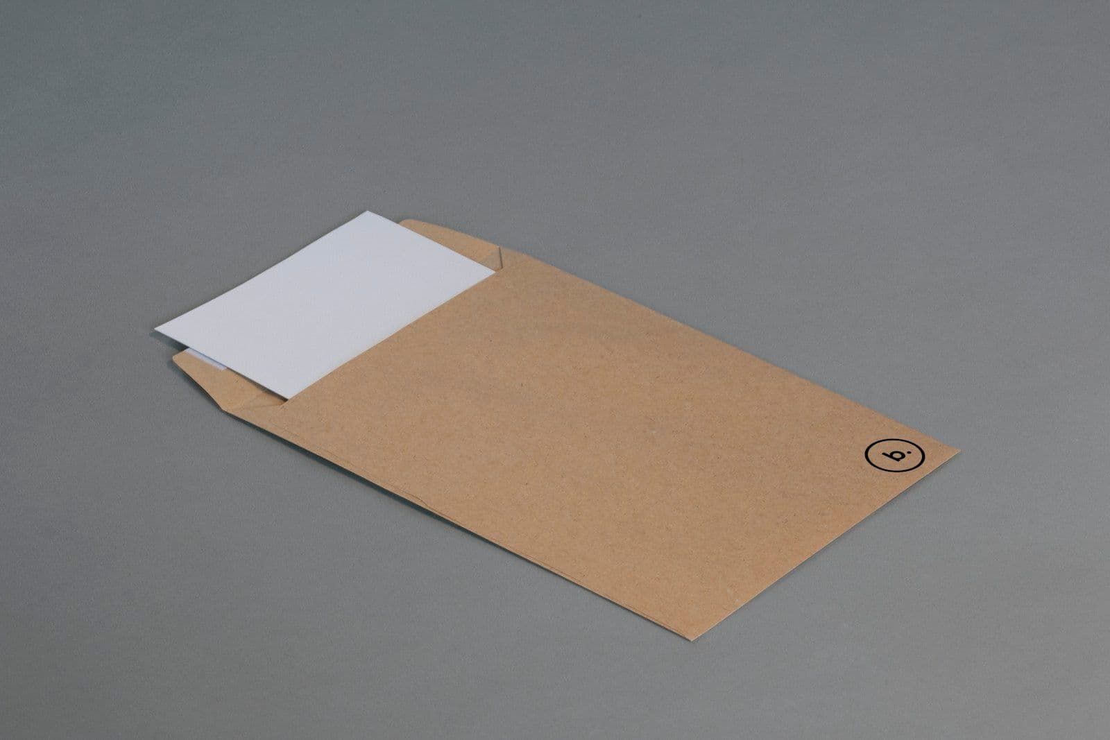 A brown kraft envelope lying flat on a gray surface with a white letter partially slid out of its top opening, with a small circular emblem printed on the lower right.