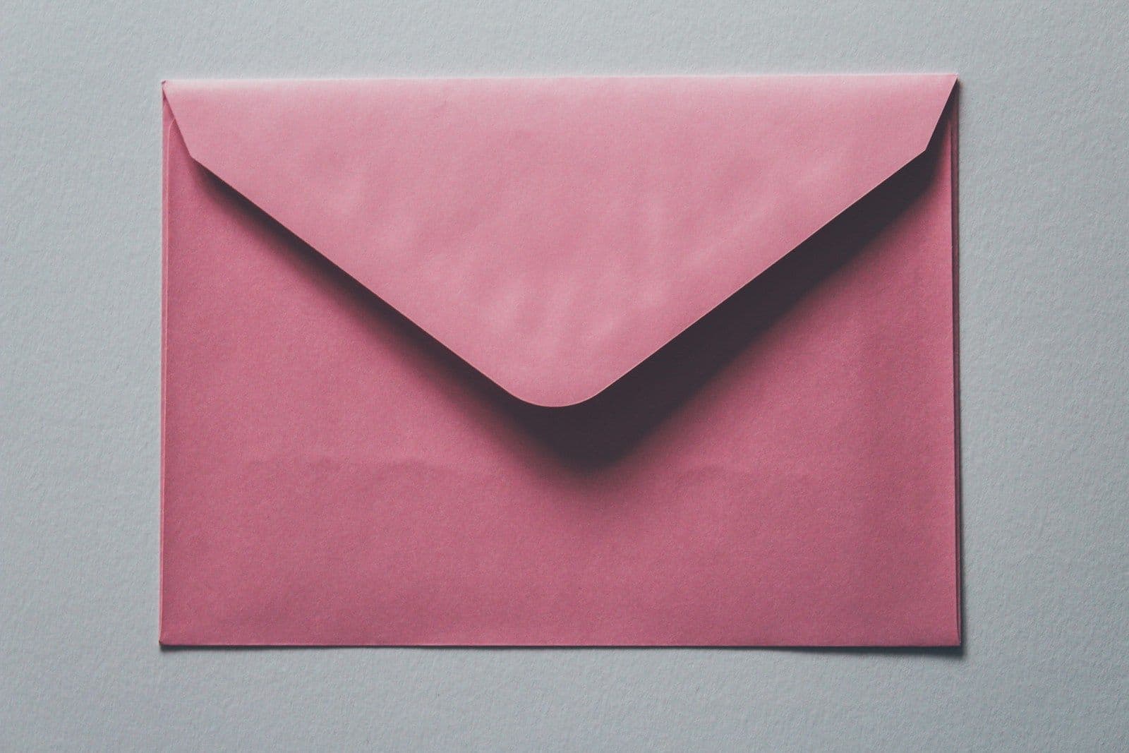 A pink envelope with a V-shaped flap lying closed on a plain gray surface, viewed from above