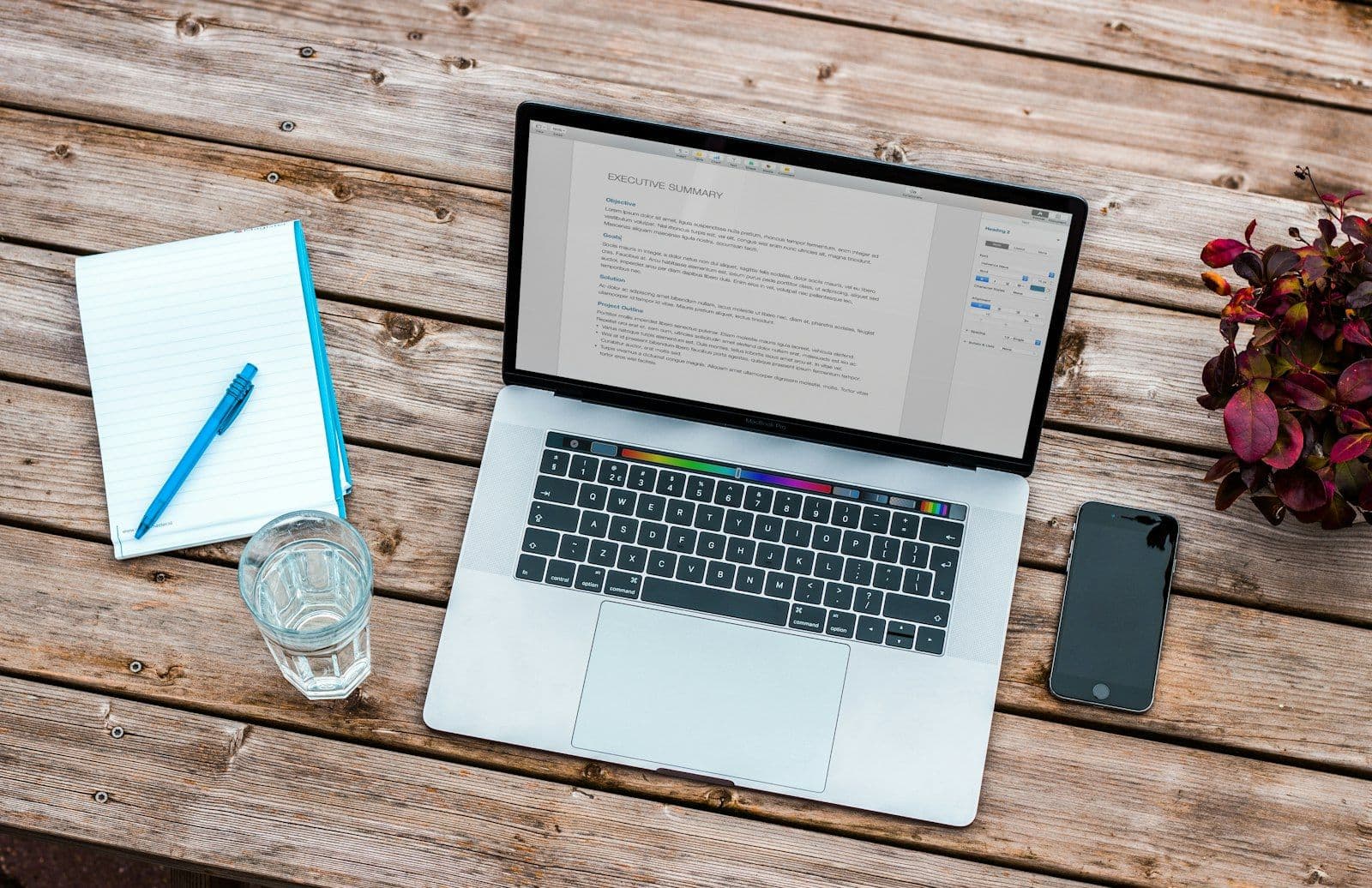 Silver MacBook beside space gray iPhone 6 and clear drinking glass on brown wooden top, illustrating how to File a CFPB Complaint.