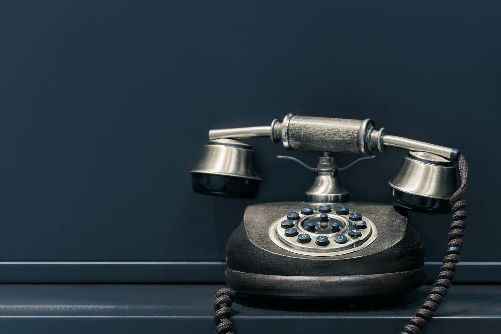 Vintage black rotary telephone with silver bell-shaped ringers and a silver handset on a dark navy background