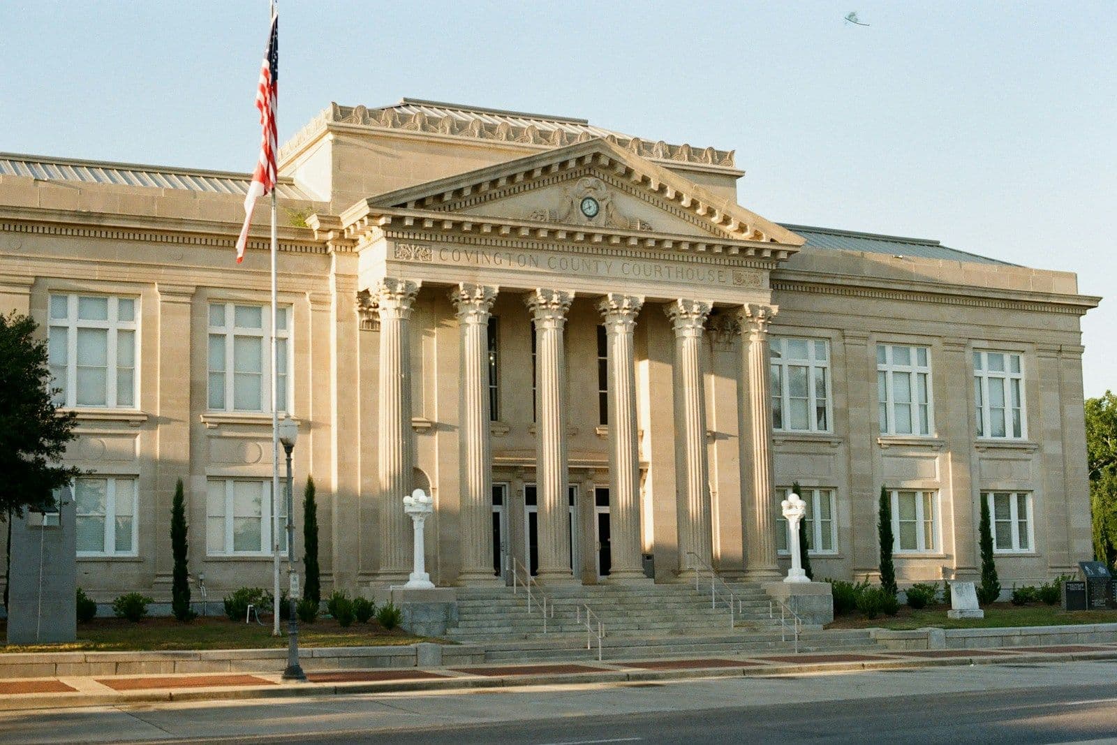 Neoclassical stone courthouse with columns, a triangular pediment, and an American flag flanking the entrance steps