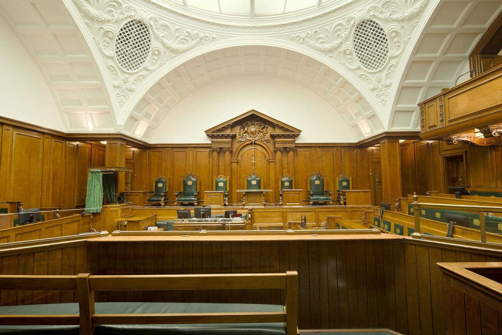 An empty wood-panelled courtroom under a domed ceiling