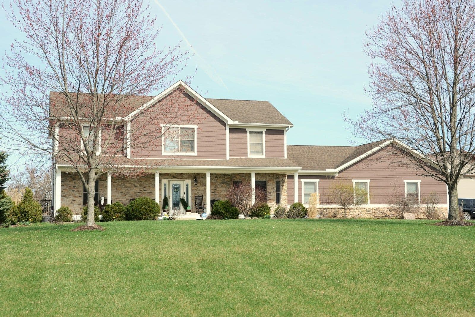 Two-story brick home with a covered front porch, white columns, and a manicured green lawn, with bare trees and a parked car beside an attached garage