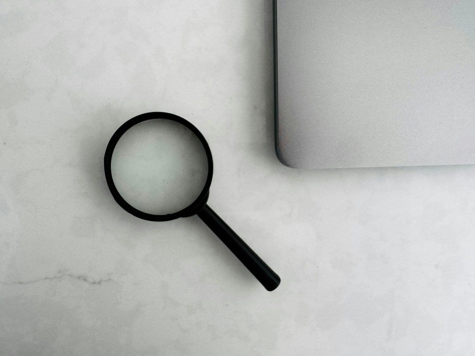 Magnifying glass sits near a laptop on a table, illustrating do Hard Inquiries Hurt Your Credit Score.
