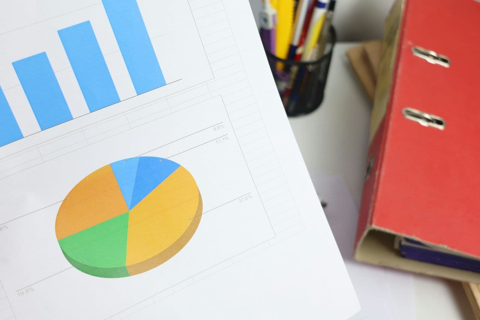 Bar and pie charts on paper with pens and a binder on an office desk