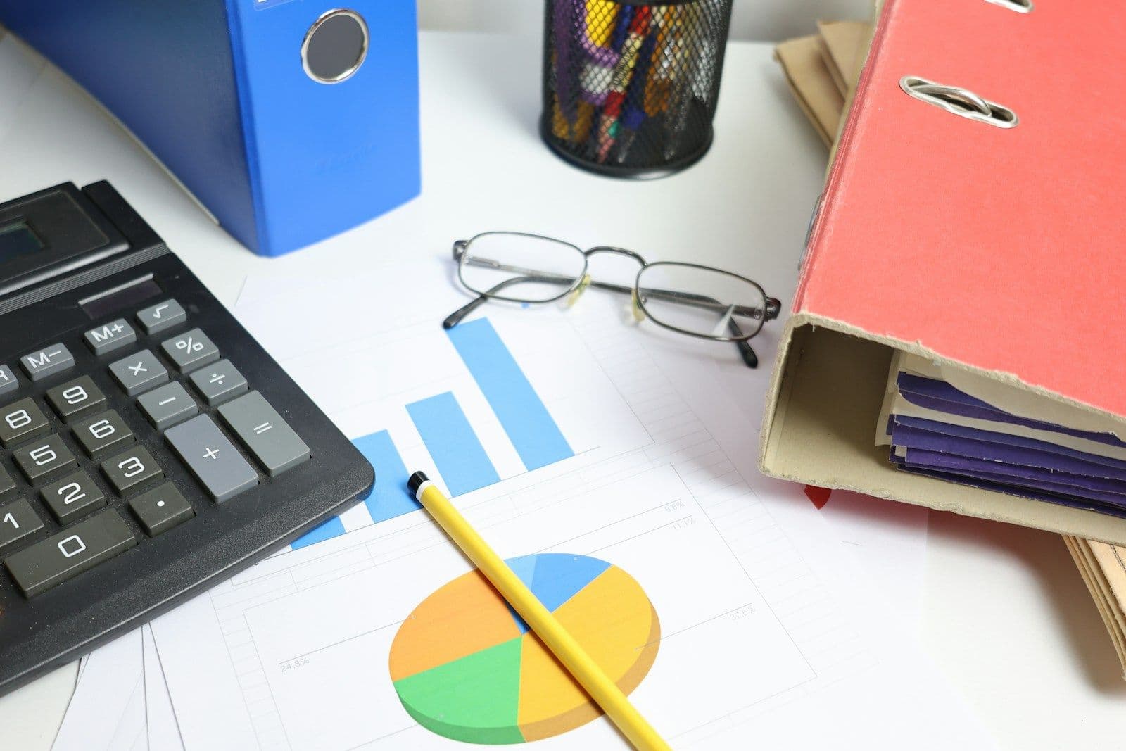 Desk with a calculator, eyeglasses, a pencil, binders, and printed bar and pie charts representing financial data analysis
