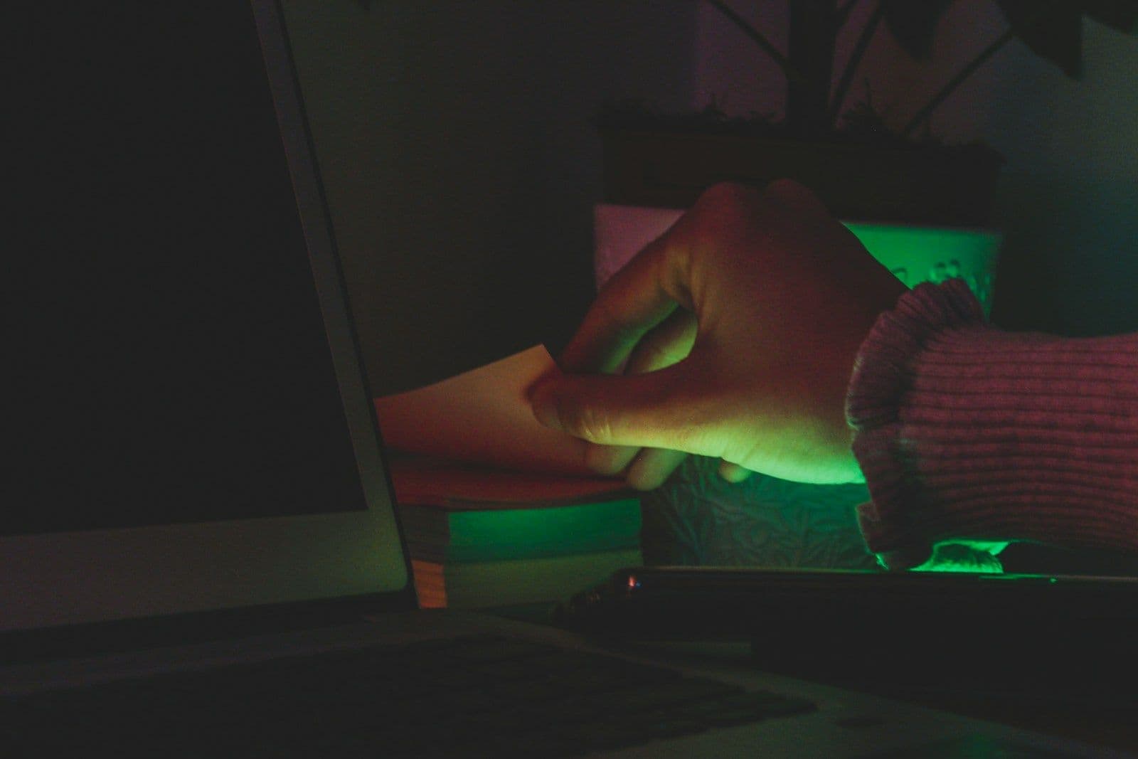 A hand reaching past a laptop in a dark room at night