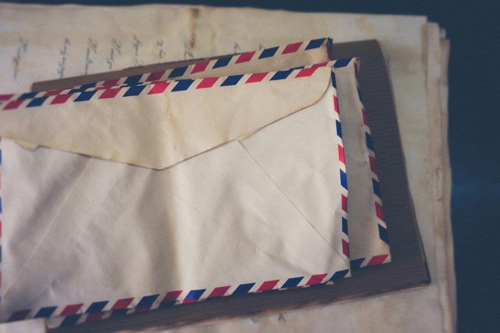 Vintage cream airmail envelope with red and blue striped border sitting atop stacked handwritten letters on a dark surface