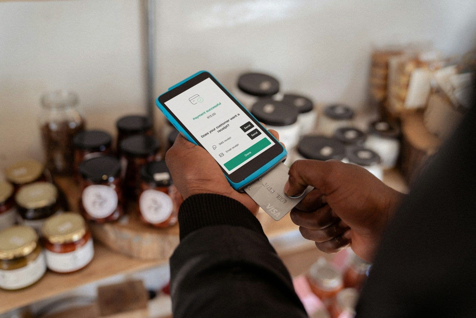 Close-up of hands holding a smartphone and a card while making a payment at an outdoor market stall