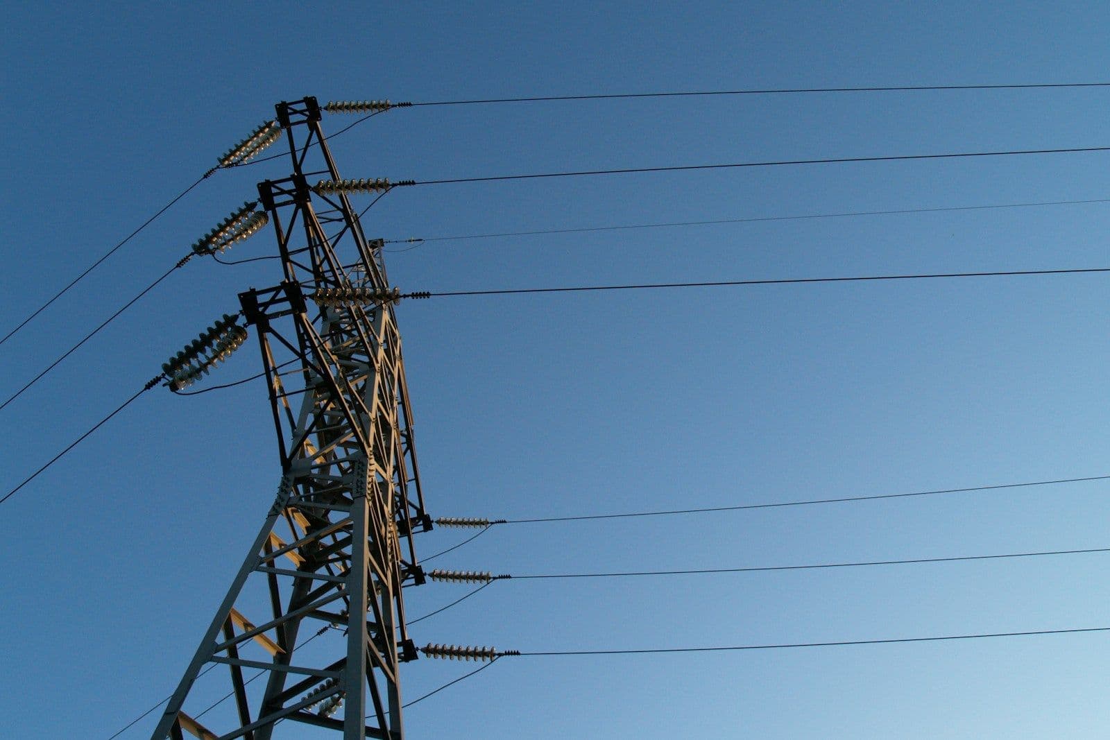 A tall steel electricity transmission tower with insulators and power lines stretching across a clear blue sky