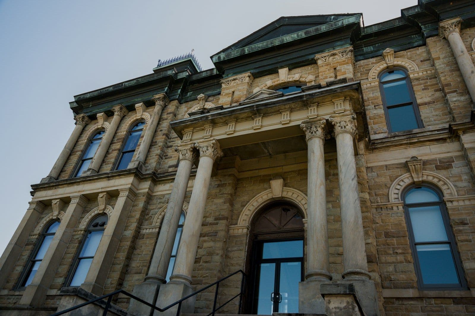 Low-angle view of a stone courthouse-style building with tall columns, arched windows, and a pedimented entrance under a clear sky