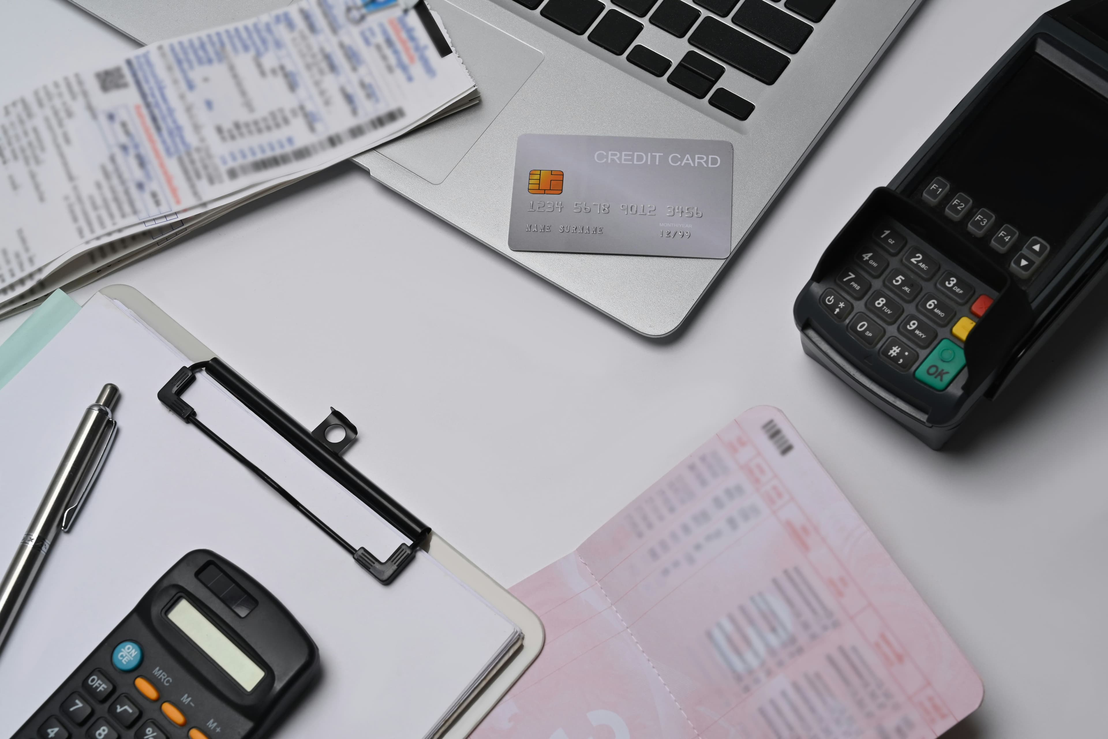Credit card on a laptop with receipts, a calculator, a clipboard, and a card terminal nearby.