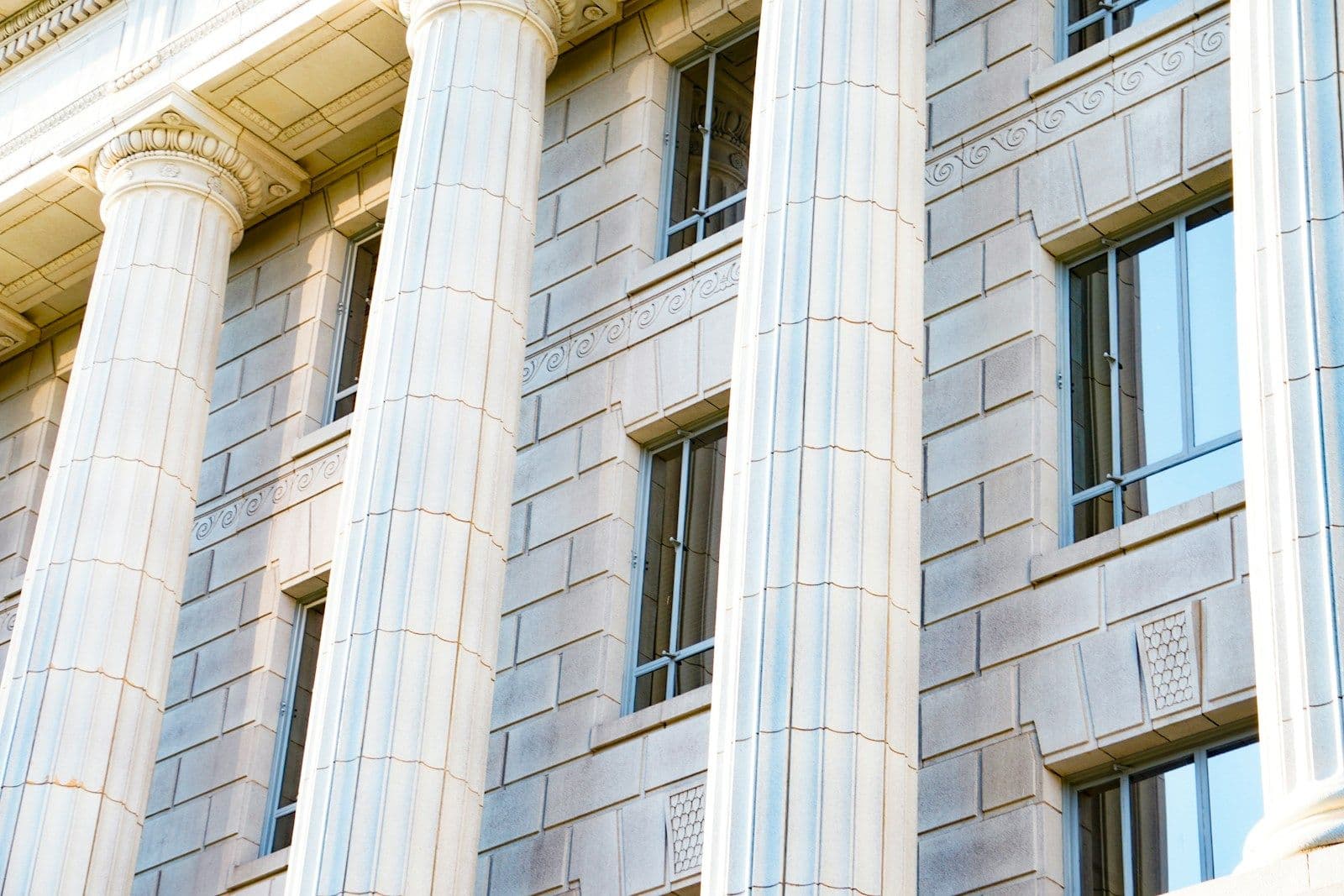 Close-up of a classical stone courthouse facade with fluted white columns, stone block walls, and tall windows in the afternoon light