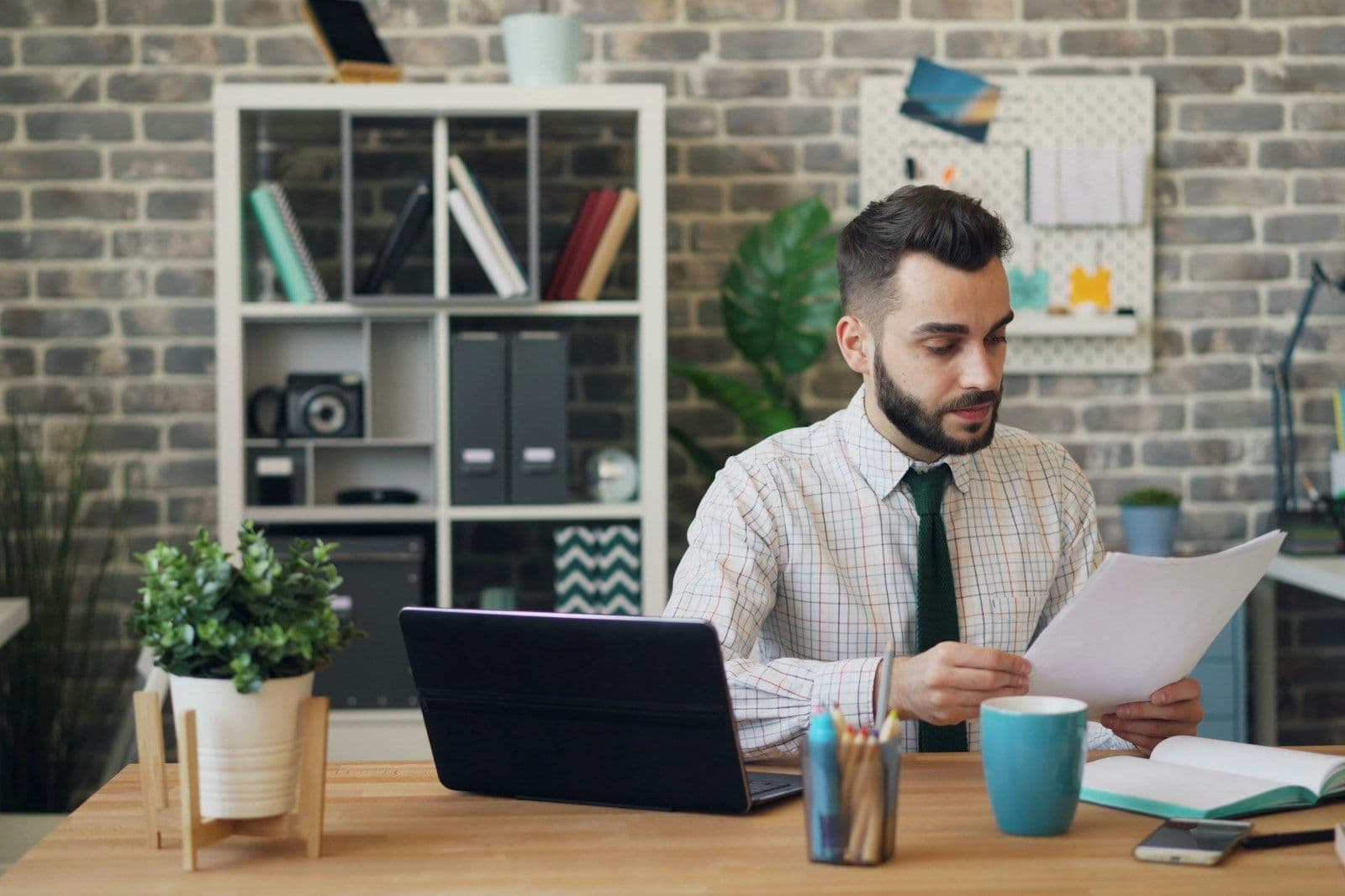 Man at office desk reviewing a document near a laptop and coffee cup