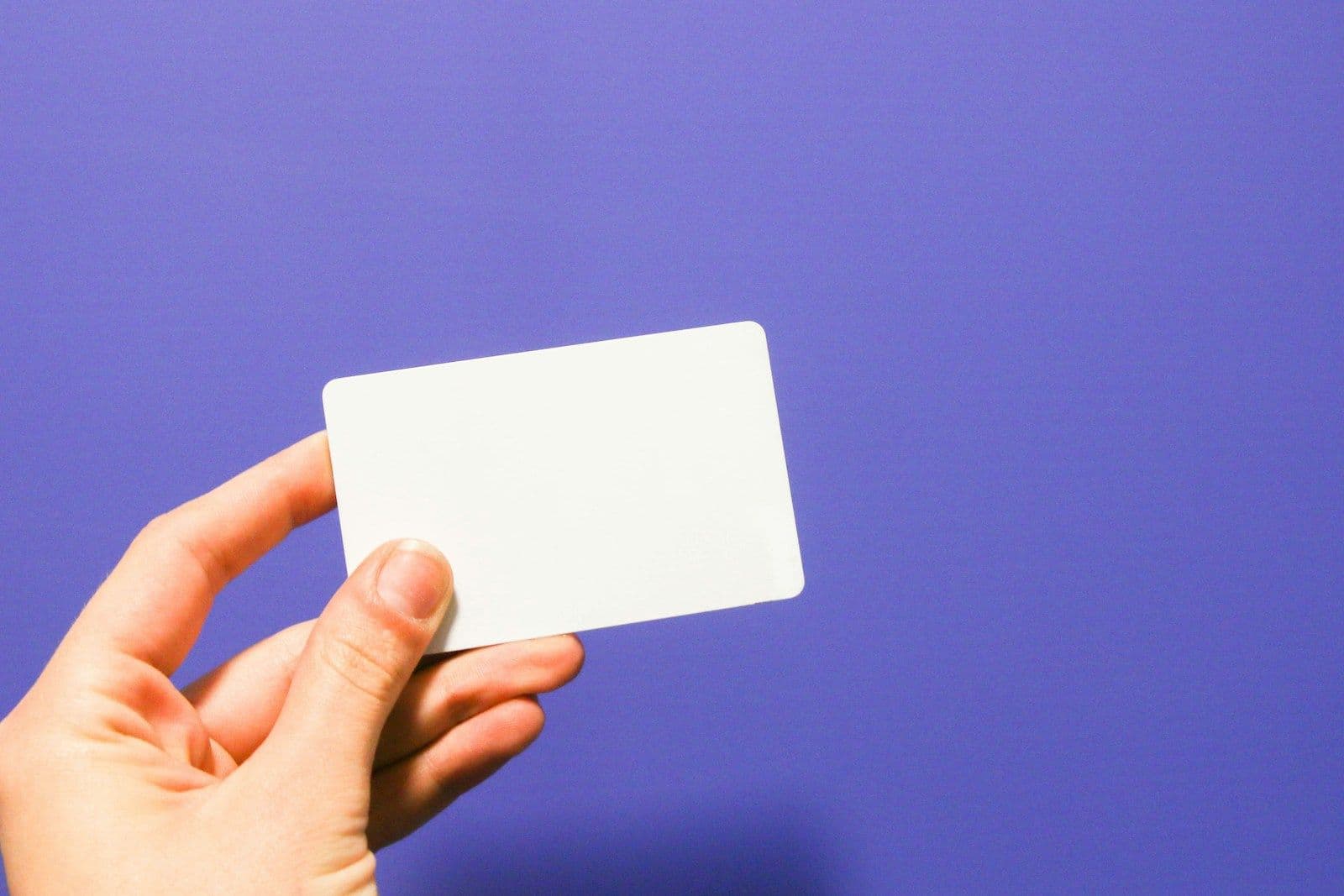 Hand holding a plain blank credit card against a purple background
