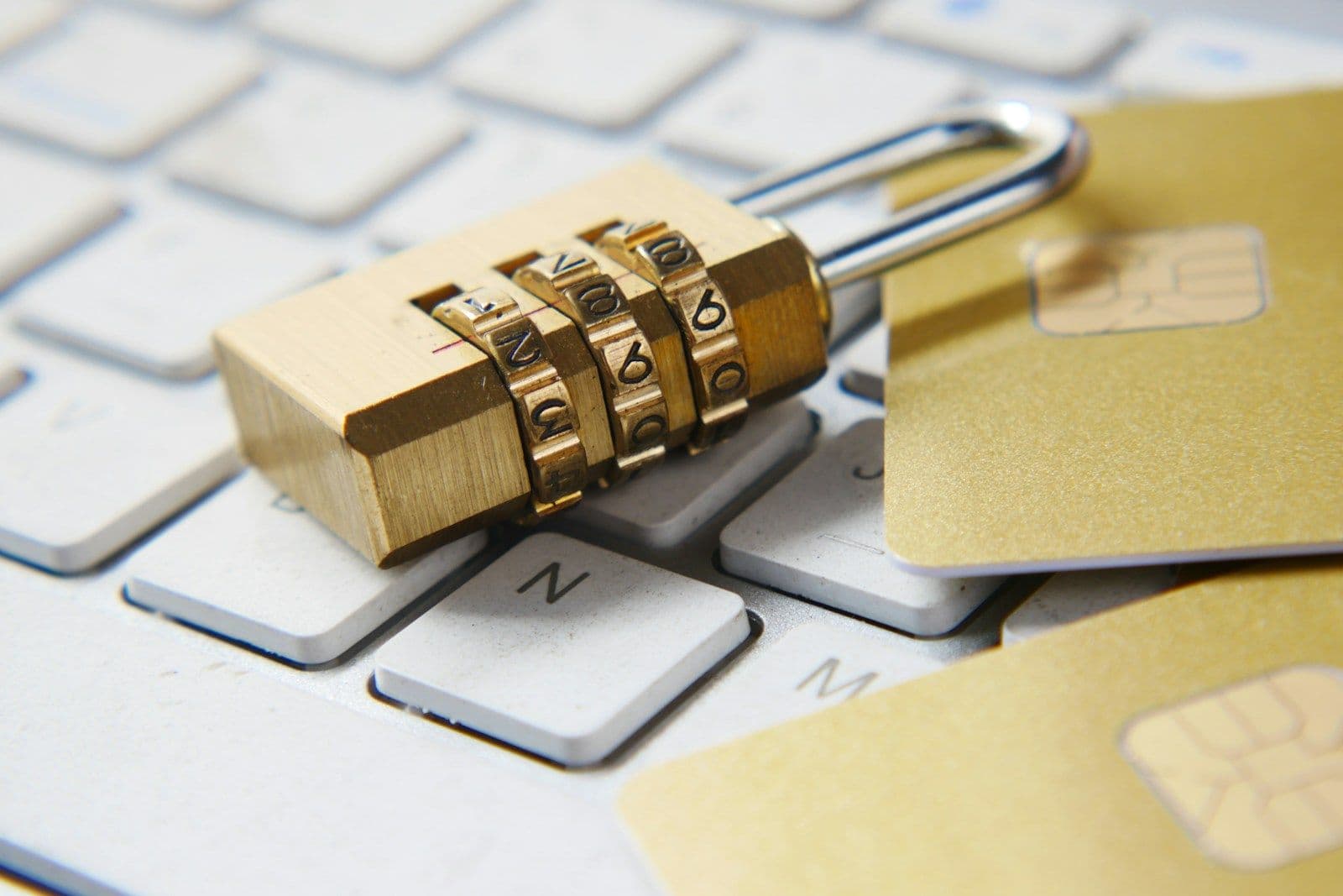 Gold combination padlock resting on a keyboard beside gold credit cards with chip visible, suggesting online financial security