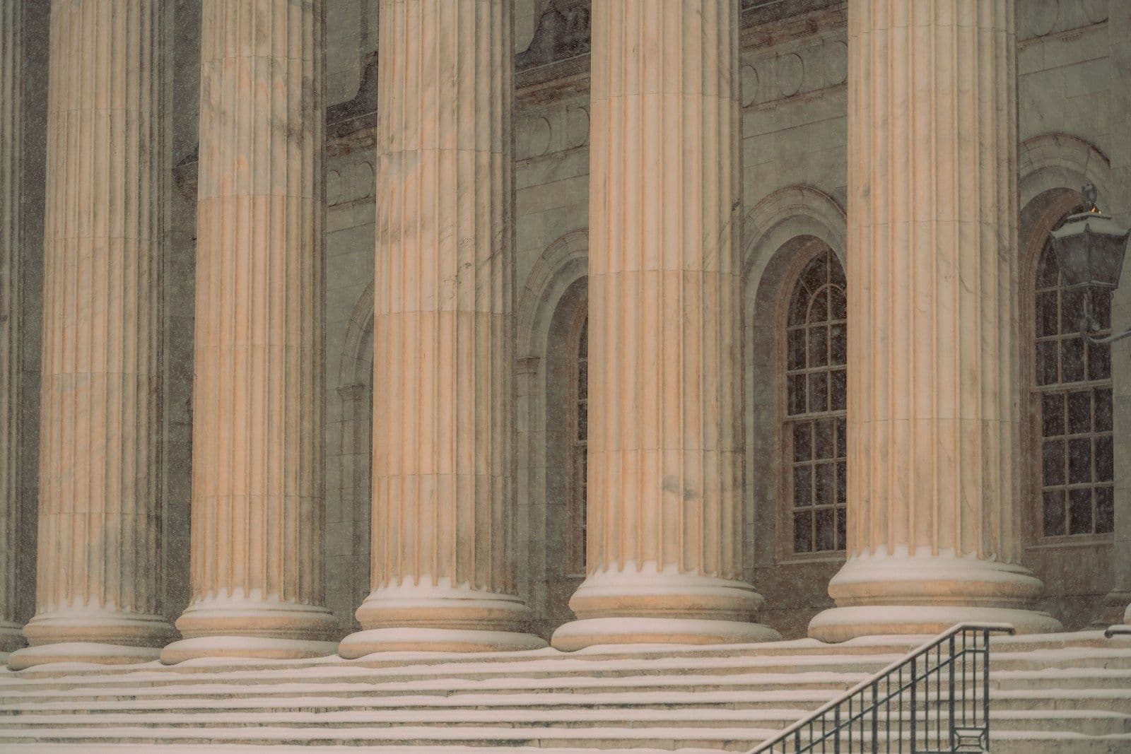 Tall fluted stone columns and granite steps with a metal handrail at the entrance of a classical courthouse-style building.