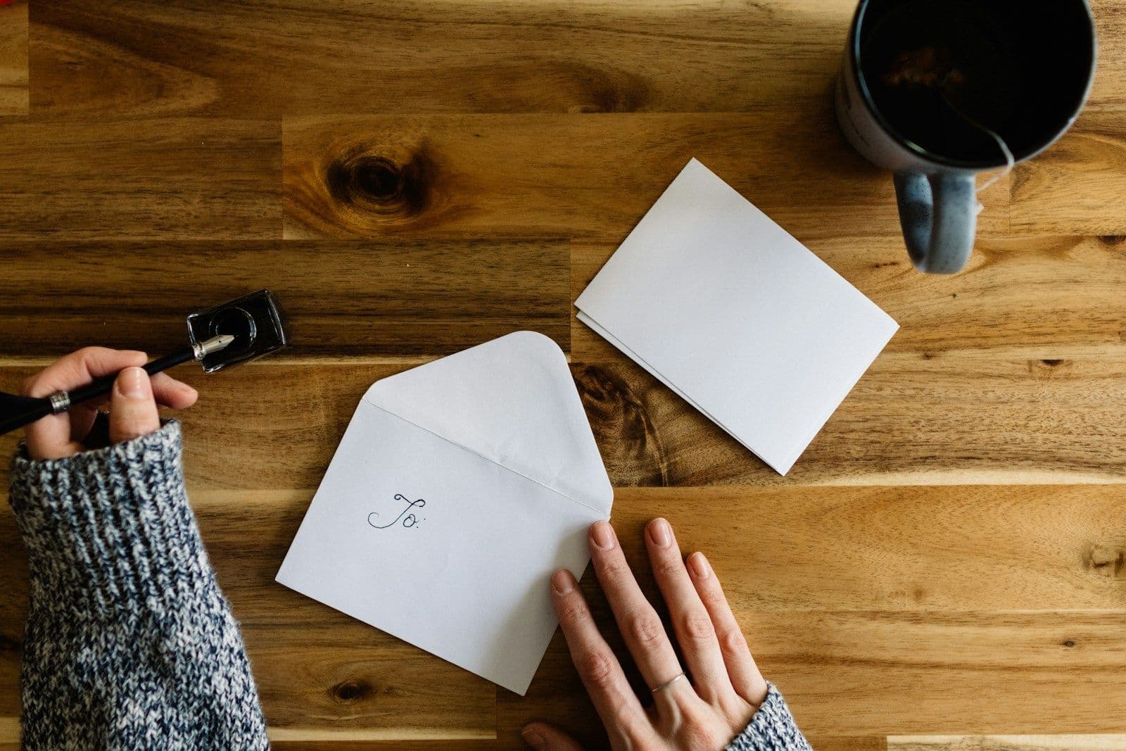 Person at a wooden table sealing an envelope beside a mug of coffee