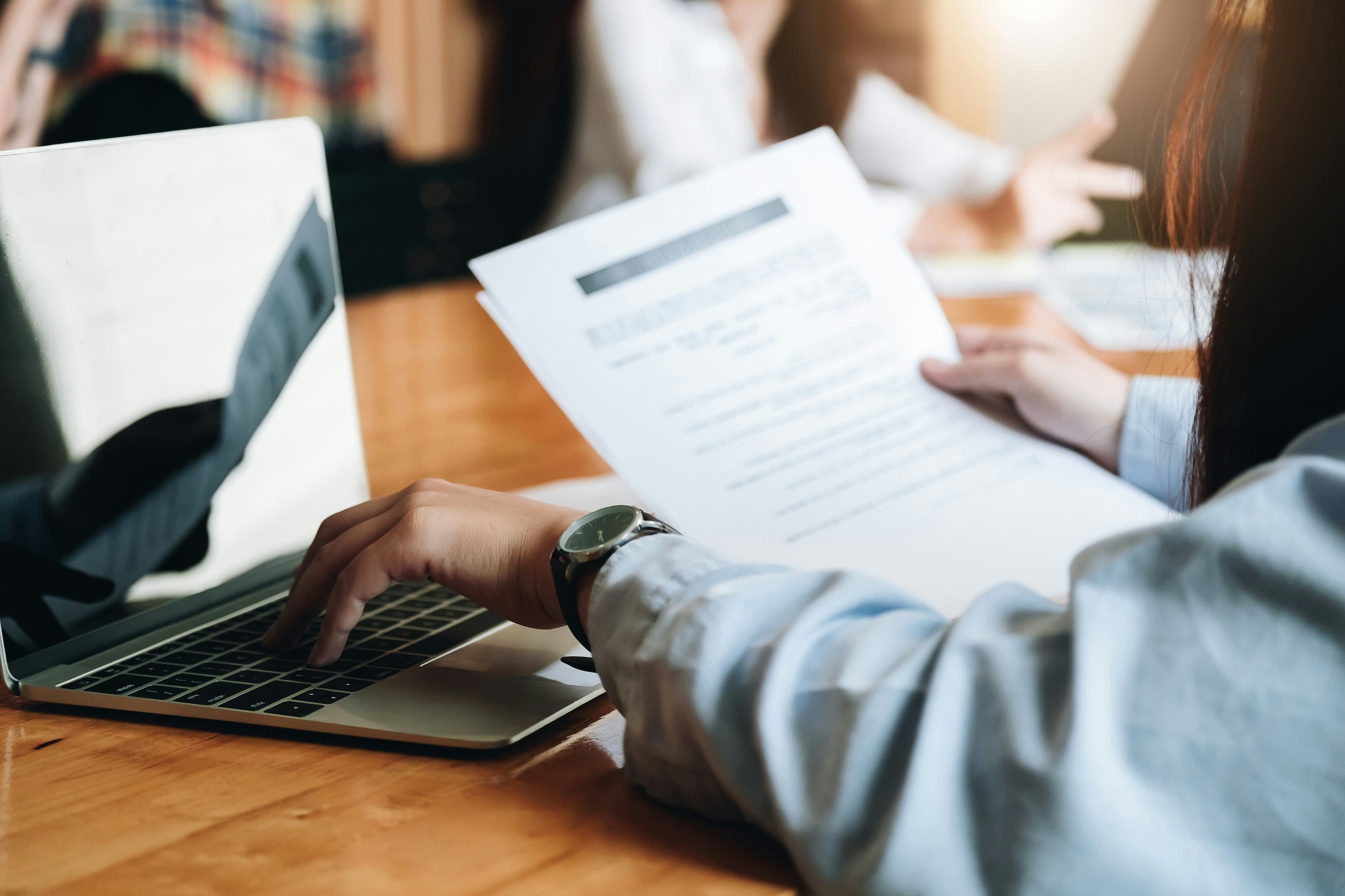 Hand typing on a laptop while holding a printed document in warm light.