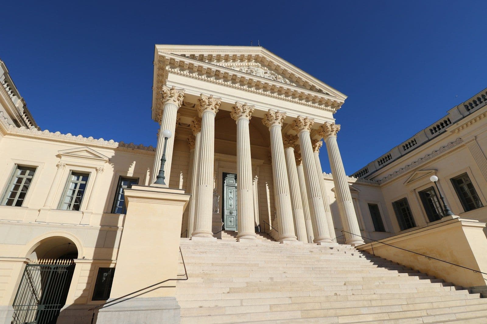 Neoclassical building with a white columned portico, triangular pediment, and wide stone staircase under a clear blue sky