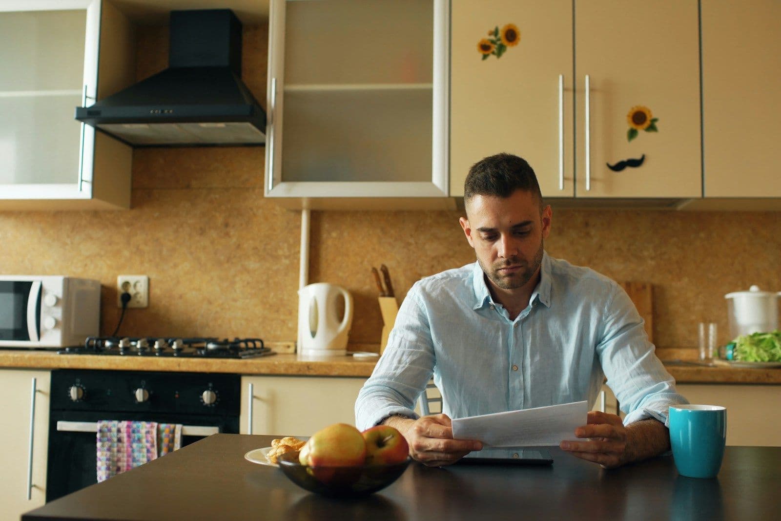 A man reads a letter at his kitchen table with a cup of coffee and a bowl of fruit