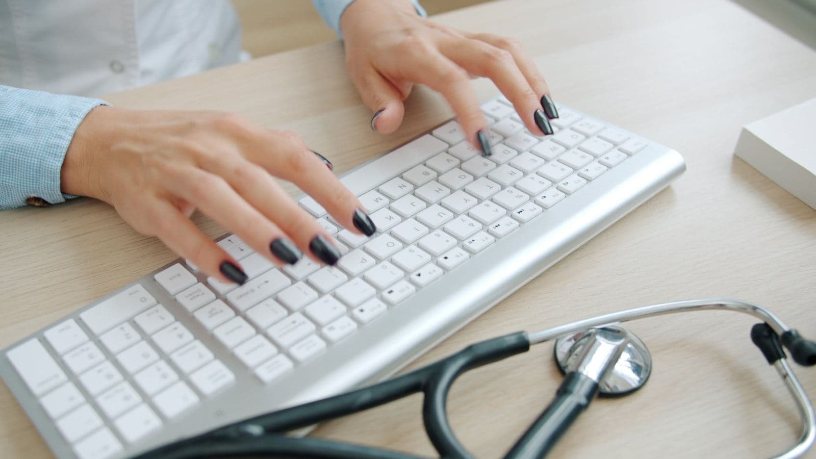 Doctor typing on keyboard with stethoscope nearby, illustrating does Medical Debt Affect Credit Score in 2026.