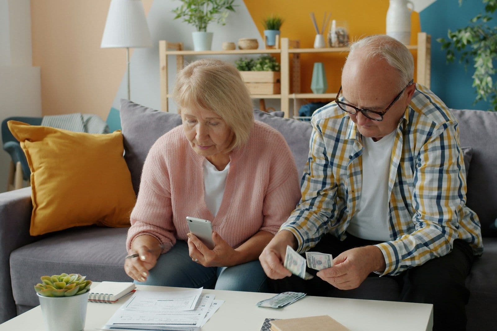 An older couple on a sofa going over bills and cash together